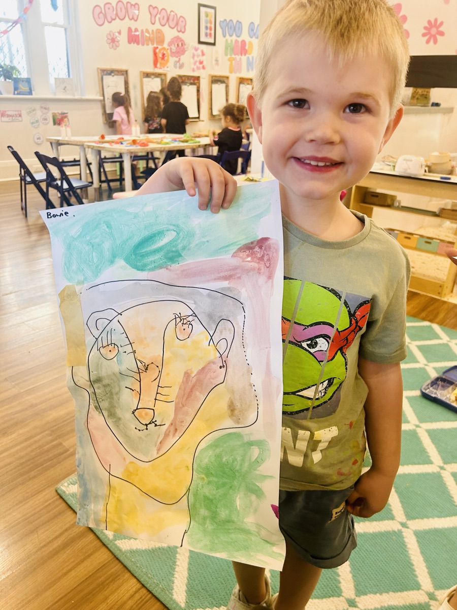 A child holding up a watercolour portrait they painted at Mini Ivy