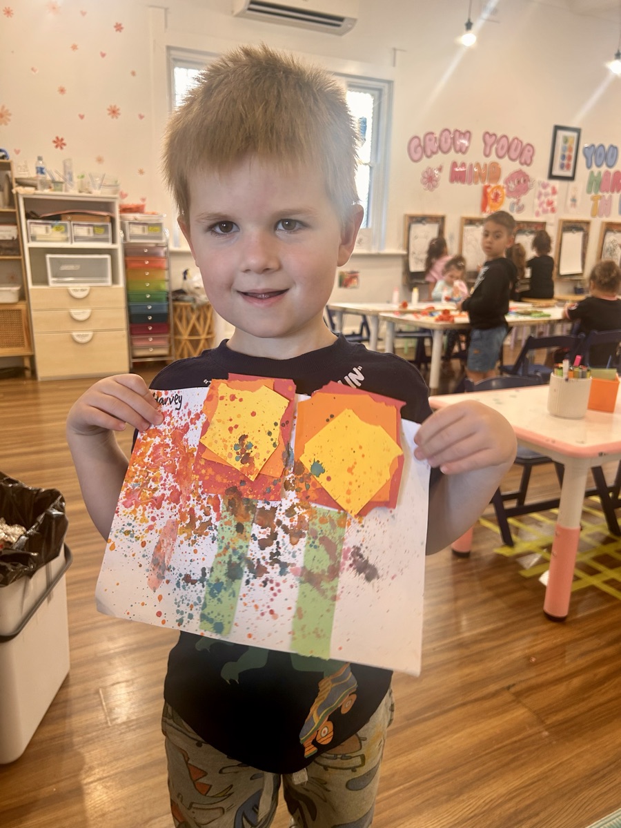 A child proudly showing off a colourful splatter and collage artwork