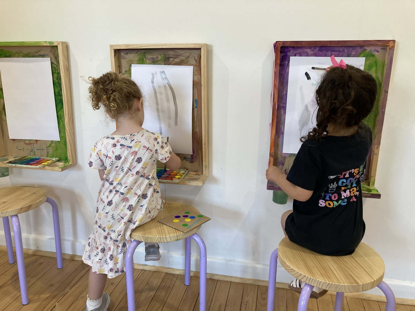 Two children painting side by side at the wall easels at Mini Ivy art studio