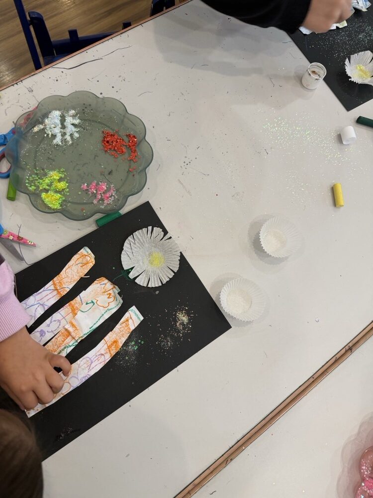 Collage strips with a paper doily and glitter on black paper