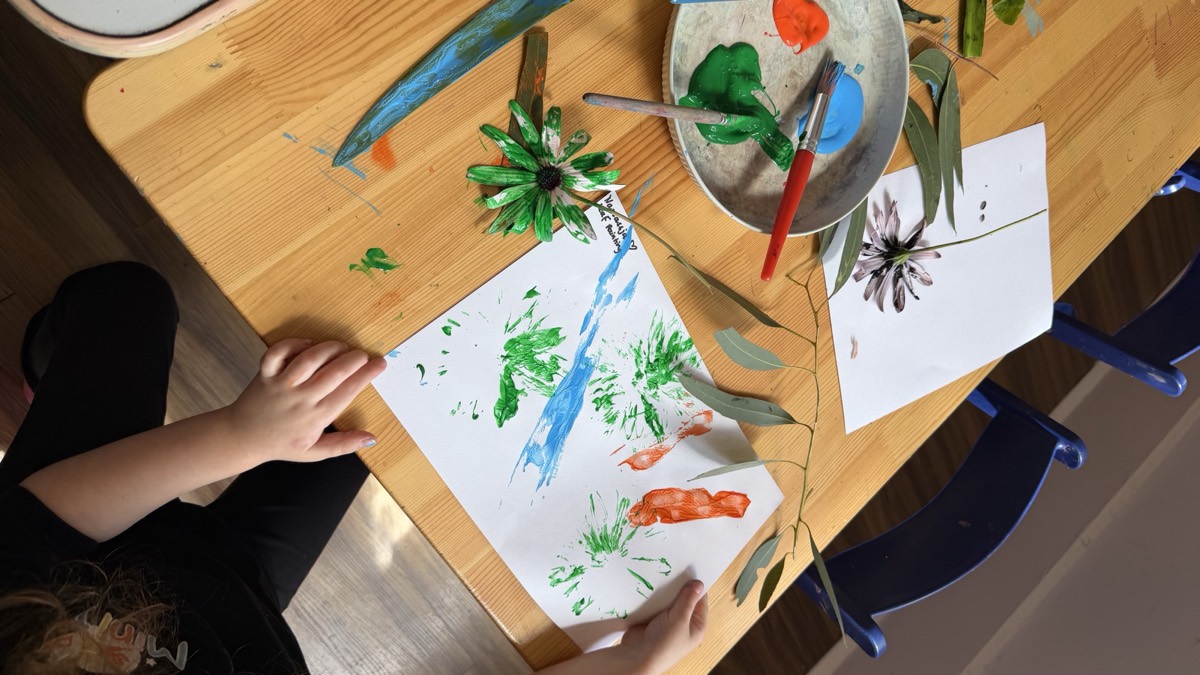 Children printing with leaves and flowers in green and orange paint