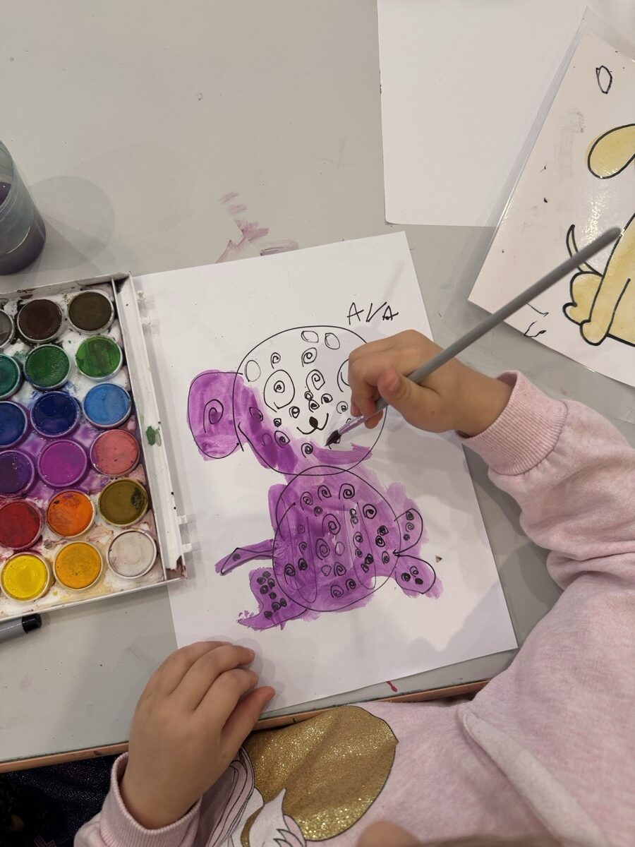 A child painting a purple dog in watercolour beside a full palette of colours