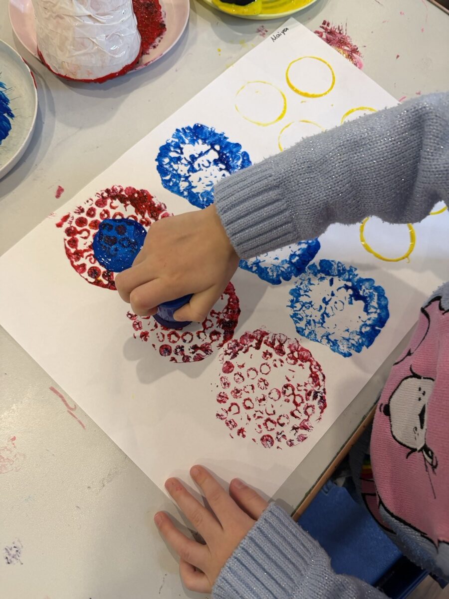 A child's hands printing rows of red and blue circles onto paper